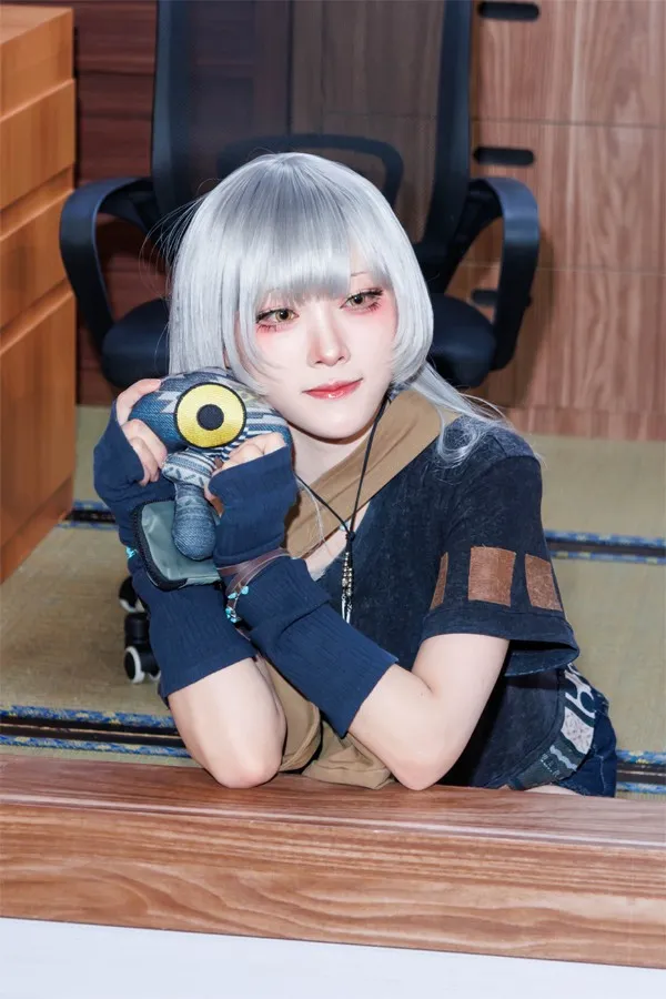 Model Aruku smiles while hugging the one-eyed mascot doll from the new work, leaning against the booth railing.