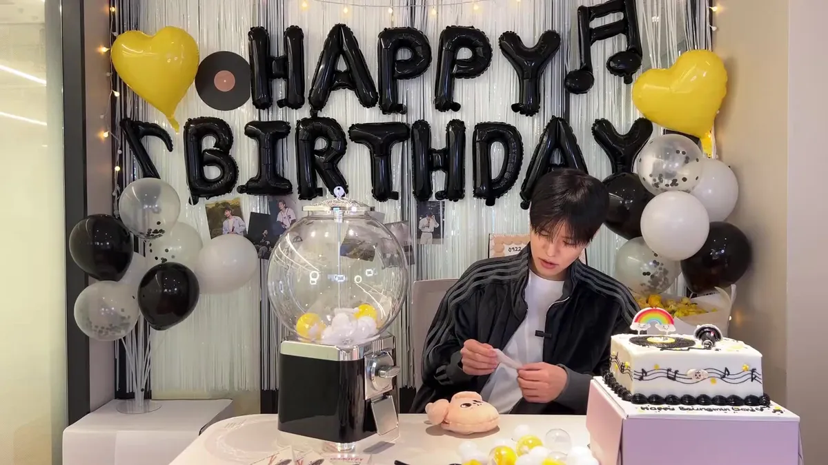Seungmin sits before a cake in front of birthday decorations