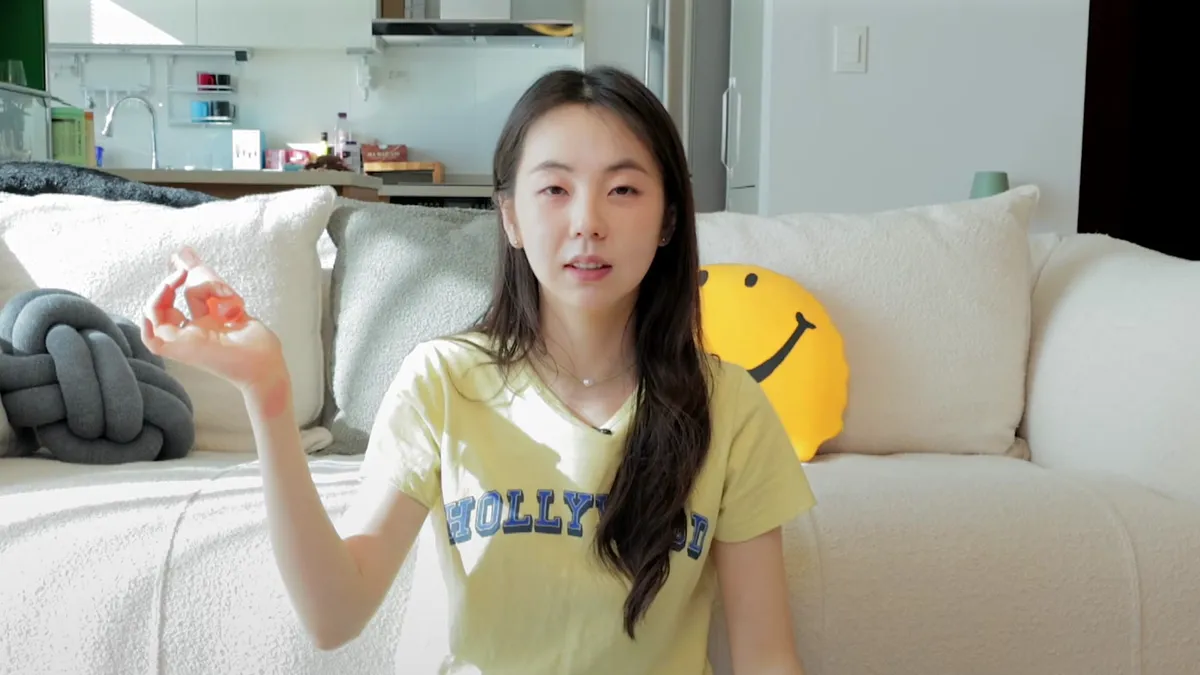 Ahn So-hee sits on a living room sofa, showcasing recommended products from Olive Young