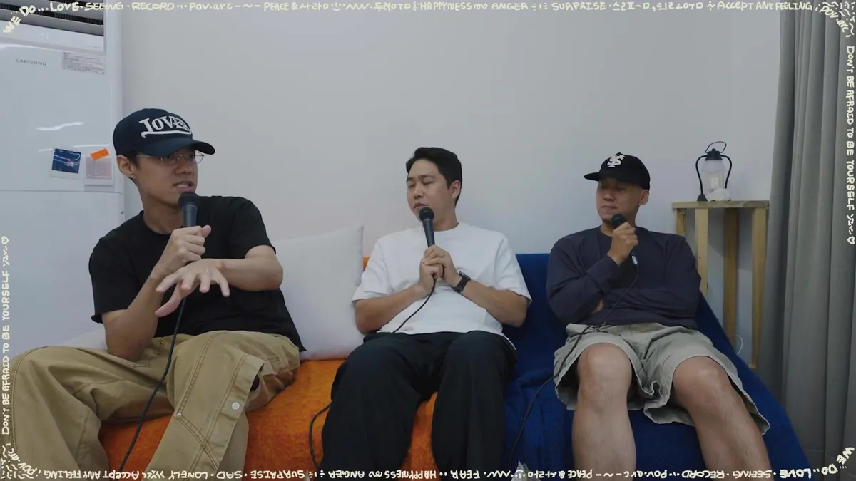 Three men sit on a sofa, holding microphones and engaging in conversation